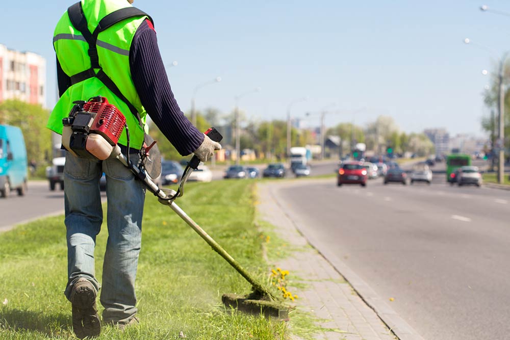 Man with lawn trimmer working on side of road